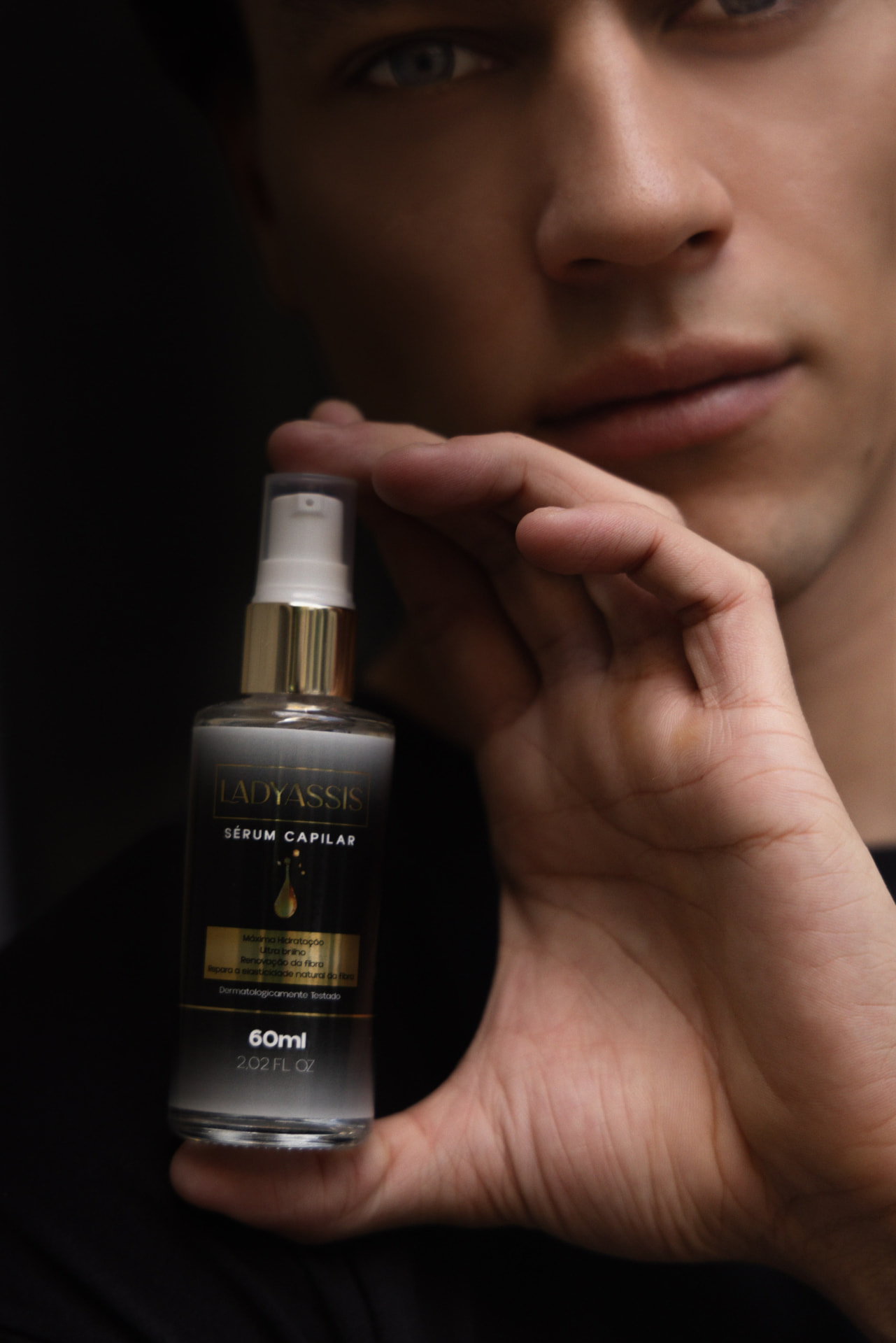 Frasco de sérum capilar LadyAssis sustentado pela mão, com o modelo ao fundo